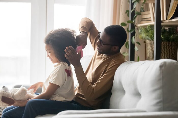 Father brushing daughter's hair on couch