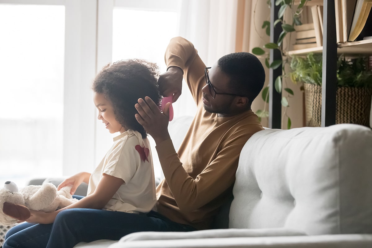 Father brushing daughter's hair on couch